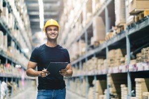 smart indian engineer man wearing safety helmet doing stock tick check and cardboard stock product management in factory warehouse background scaled